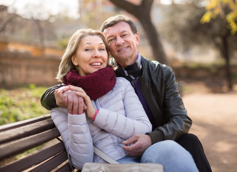 Happy aged lovers on a bench in the park in autumn day